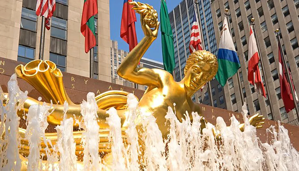 The image showcases a golden statue of Prometheus in front of a fountain with international flags flying in the background at Rockefeller Center in New York City