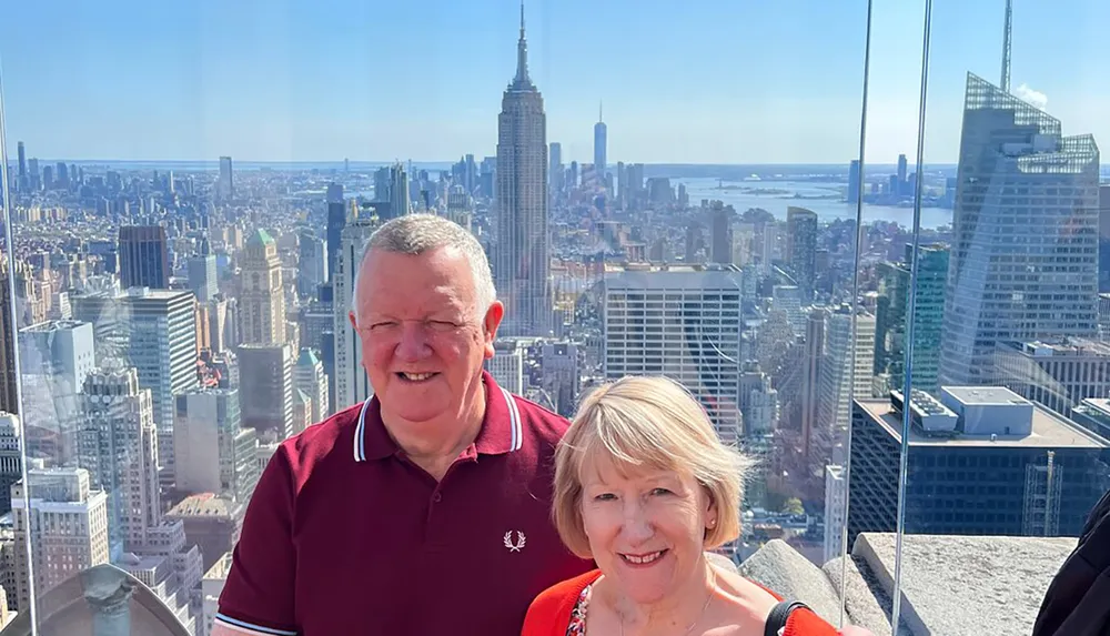 A smiling couple poses for a photograph with the New York City skyline including the Empire State Building in the background