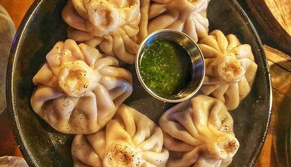The image shows a pan of delicately folded dumplings accompanied by a bowl of dipping sauce
