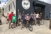 A group of people with bicycles are posing and smiling in front of the Hometown Bar-B-Que restaurant.