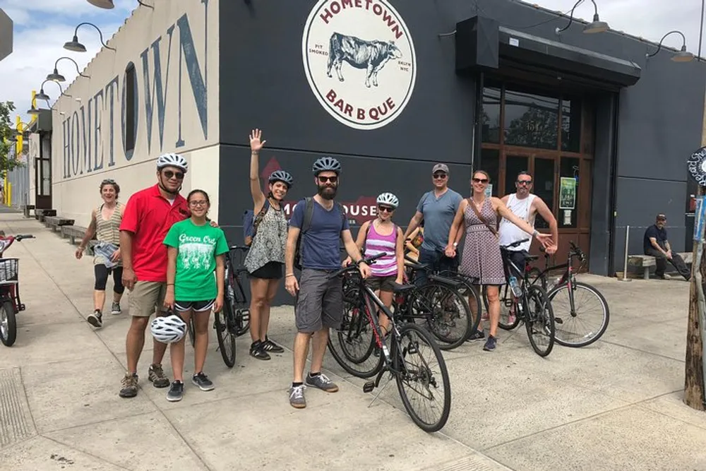 A group of people with bicycles are posing and smiling in front of the Hometown Bar-B-Que restaurant