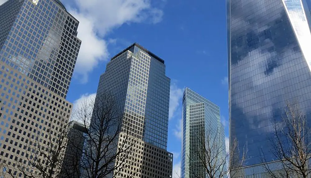 The image shows a cluster of modern skyscrapers reaching up into a clear blue sky dotted with a few clouds