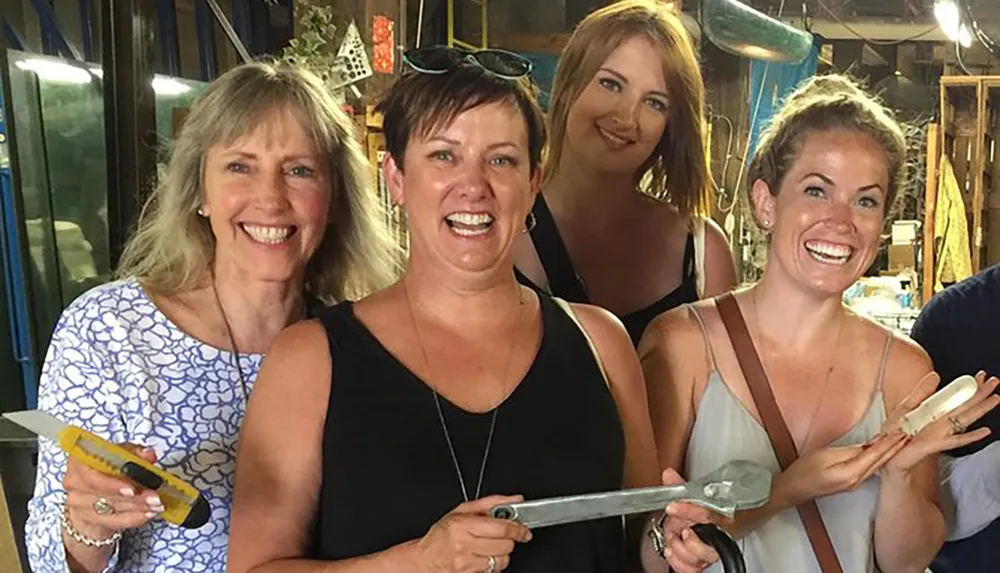 Four women are smiling for the camera while holding large sculpting chisels in a workshop setting