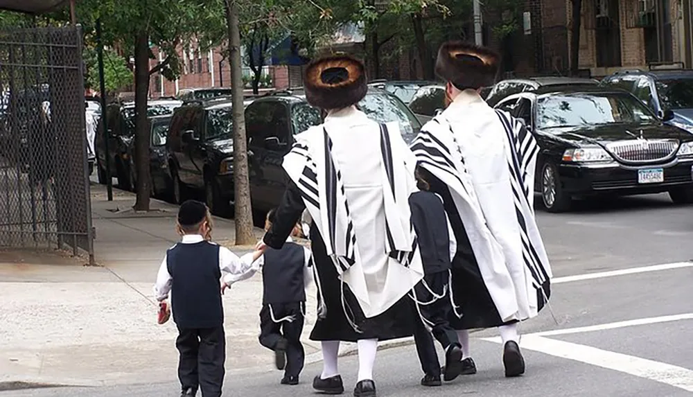 Two adults and two children dressed in traditional Hasidic Jewish attire with prayer shawls and fur hats are walking down a city sidewalk
