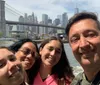 Four people are smiling for a selfie with the Brooklyn Bridge and the Manhattan skyline in the background