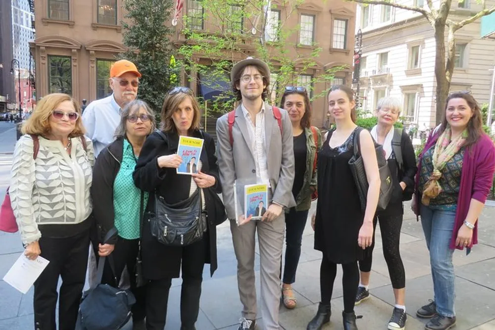 A group of people pose for a photo on a city street two of whom are holding books with visible covers