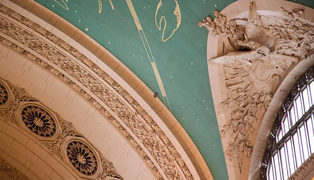 The image shows a detailed interior view of a ceiling with ornate architectural moldings and a carved sculpture featuring a vaulted section adorned with gold accents and a turquoise backdrop