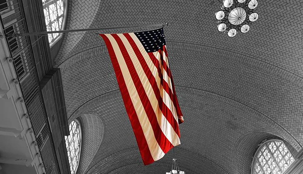 An American flag hangs vertically in a monochromatic indoor setting with its colors selectively highlighted