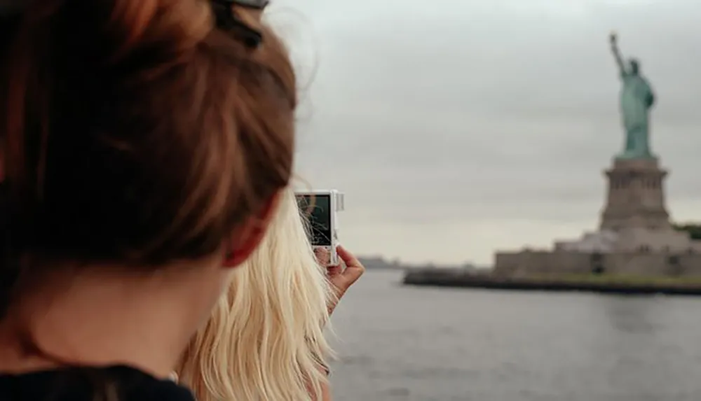 A person is taking a photo of the Statue of Liberty from a distance with a smartphone