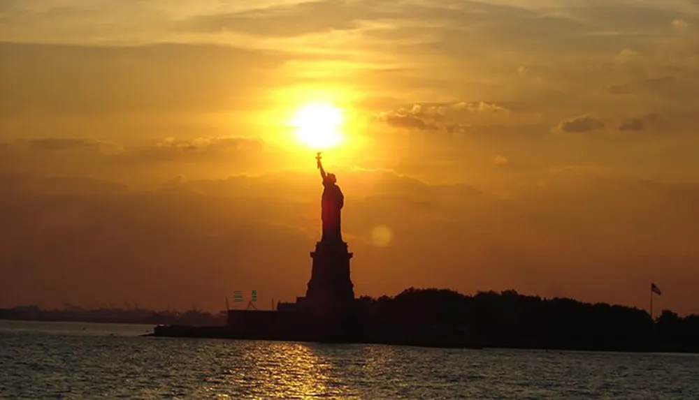 The silhouette of the Statue of Liberty is set against a golden sunset sky