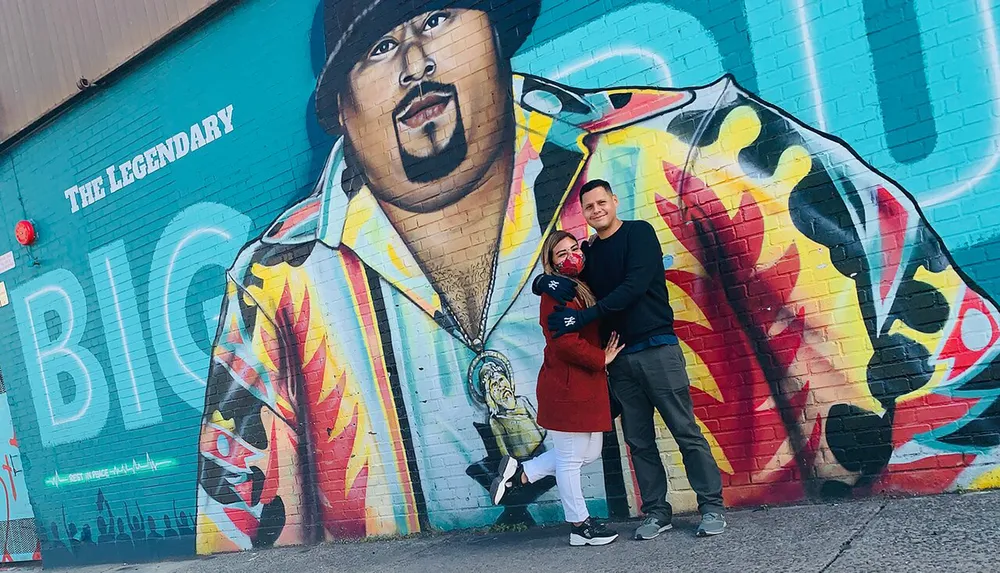 A couple is posing in front of a vibrant mural of a legendary singer