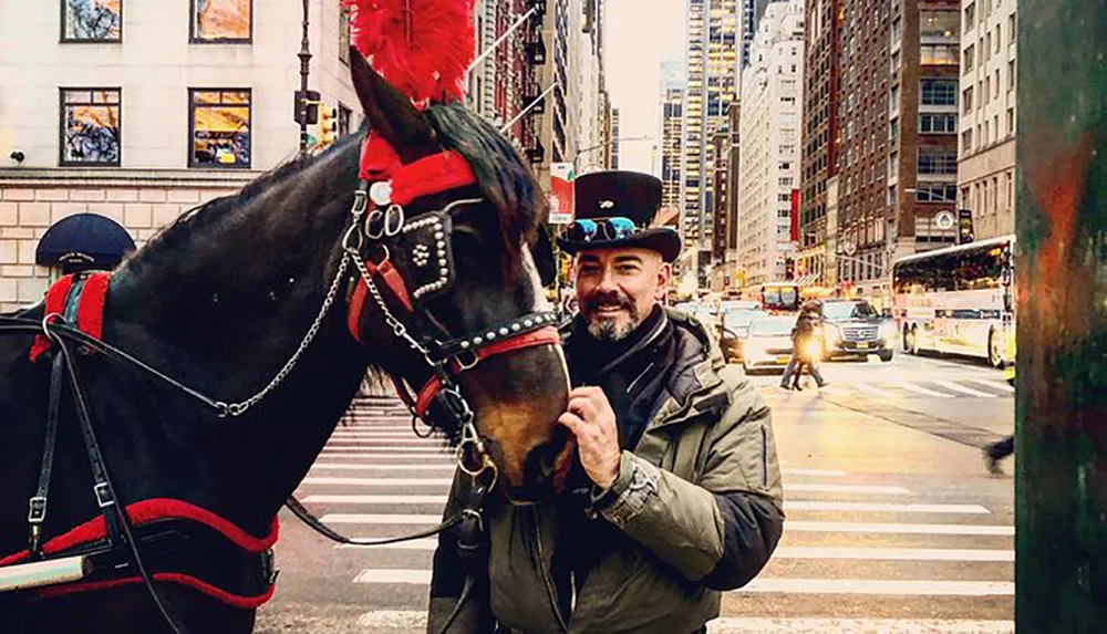 A man in a top hat smiles as he poses next to a horse adorned with festive headwear on a bustling city street