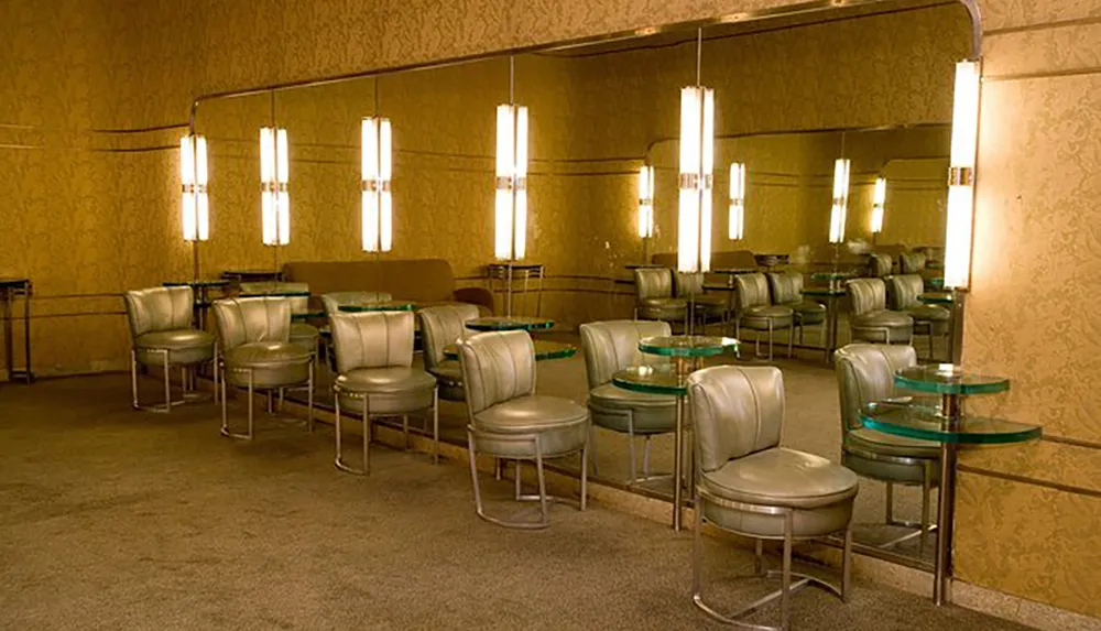 The image shows a vintage-style interior with green swivel chairs and glass tables accented by vertical wall lamps and mirrored walls evoking a retro atmosphere