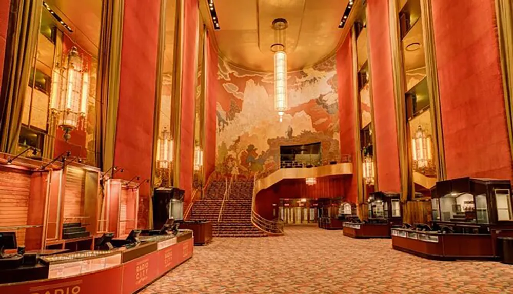 The image shows the grand opulent interior of a theater lobby with luxurious red draperies an expansive mural a wide staircase and Art Deco style design elements
