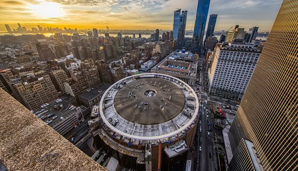 The image shows an aerial view of New York City during sunset highlighting the unique circular architecture of Madison Square Garden amidst the urban landscape