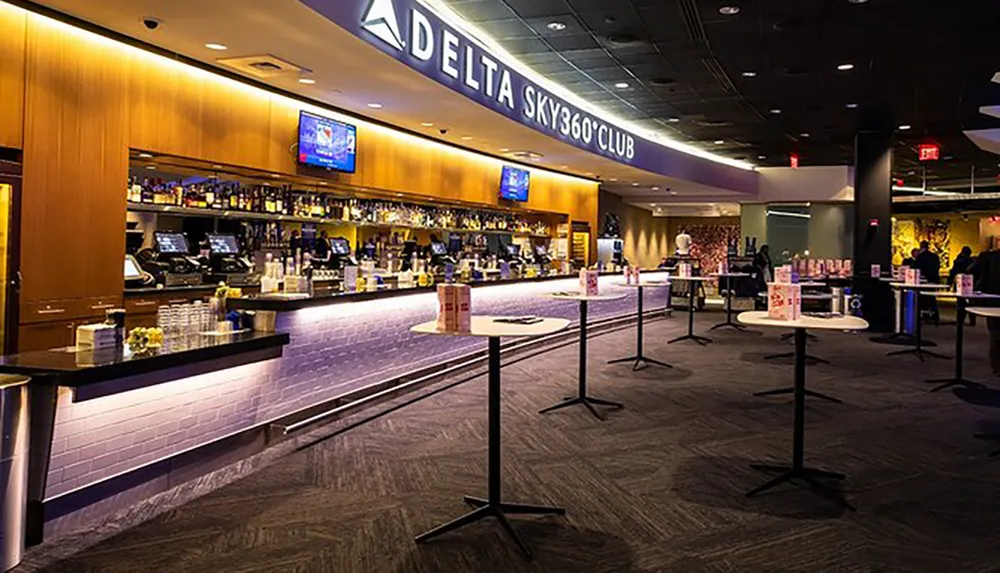 The image shows a modern bar area with the signage Delta Sky360 Club featuring a well-stocked bar counter tables with social distancing markers and a dimly lit lounge atmosphere