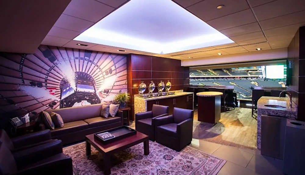The image shows a luxurious modern suite with comfortable seating a large mural of a stadium and a view onto an actual sports arena from inside what appears to be a VIP box