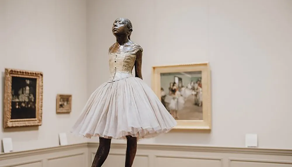 The image features a sculpture of a ballerina with a poignantly expressive pose set against the backdrop of an art gallery with framed paintings