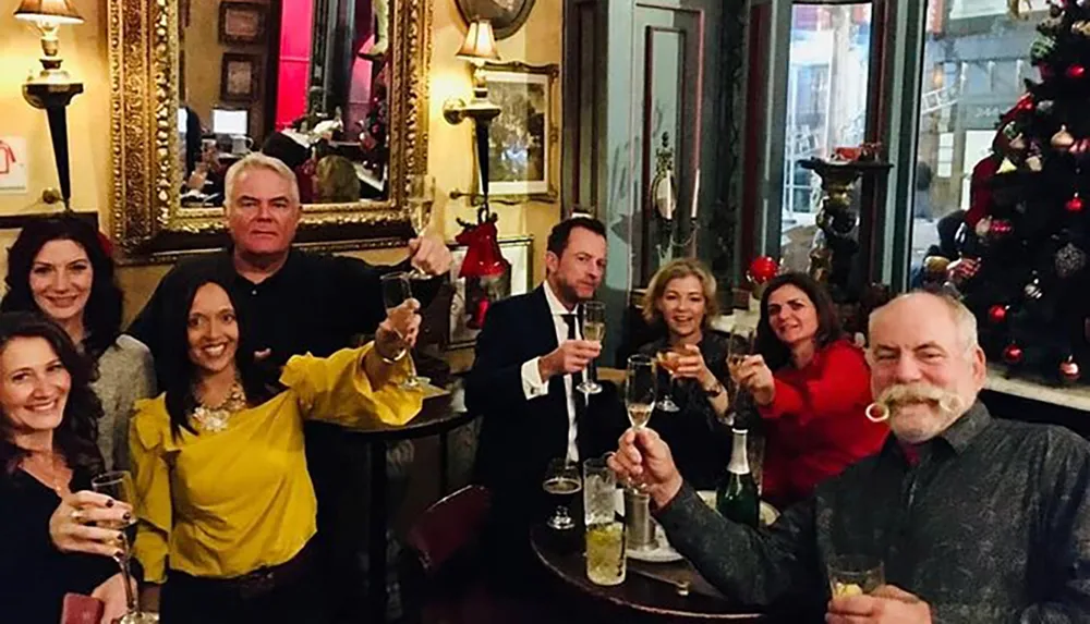 A group of people is cheerfully toasting with champagne in a decorated room with a Christmas tree in the background