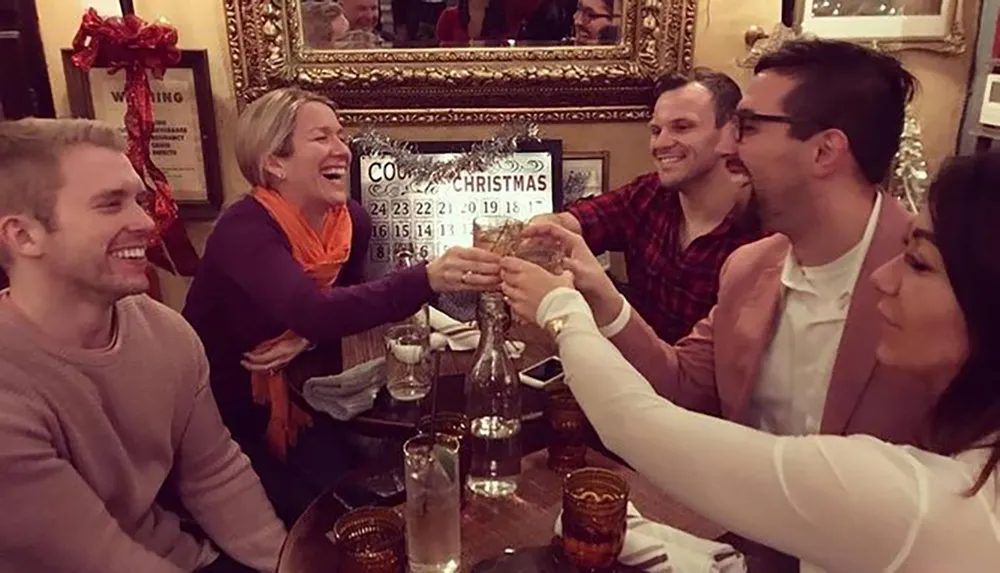 A group of people are joyfully toasting drinks around a table adorned with Christmas decorations in a festive setting
