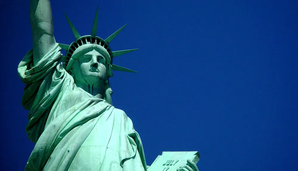 The image is a close-up of the Statue of Liberty against a clear blue sky