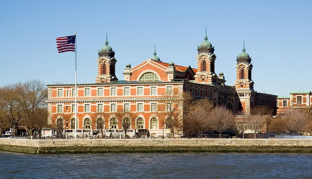 The image shows the historic Ellis Island immigration station in the United States with the American flag flying above it