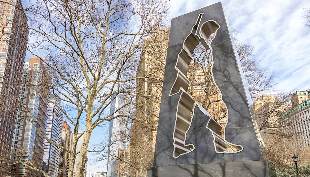 This image features an abstract cut-out metal sculpture in an urban park setting with bare trees and modern high-rise buildings in the background