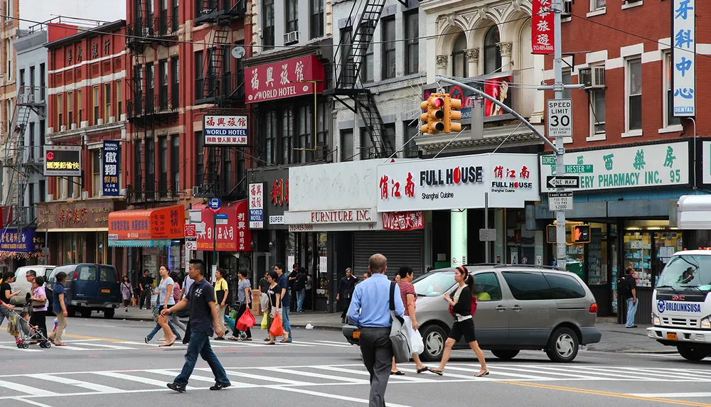 The image shows a bustling city street with pedestrians cars and multiple signs in English and Chinese suggesting a Chinatown setting in a major urban area