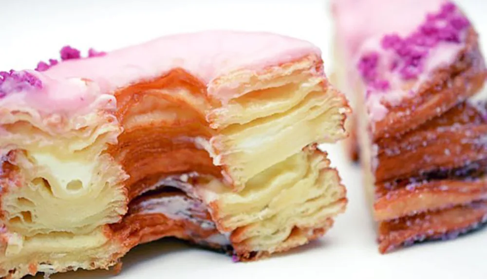 The image showcases a close-up of a sliced layered pastry with a pink icing on top resembling a cronut