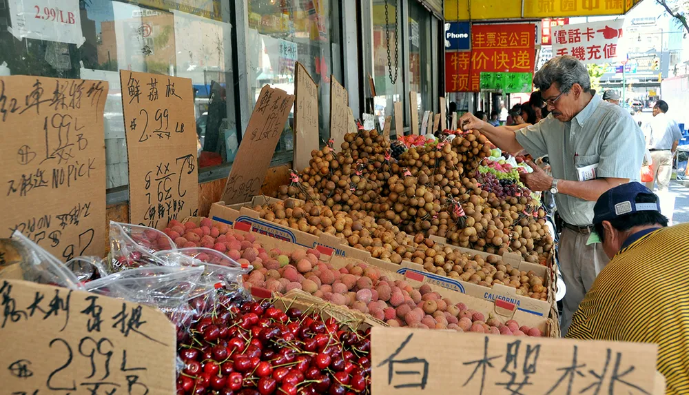 A man is selecting fruit from a pile at a bustling outdoor market with signs in Chinese characters