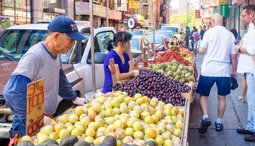 A bustling street market scene with vendors selling an array of colorful fruits with pedestrians walking by in an urban setting