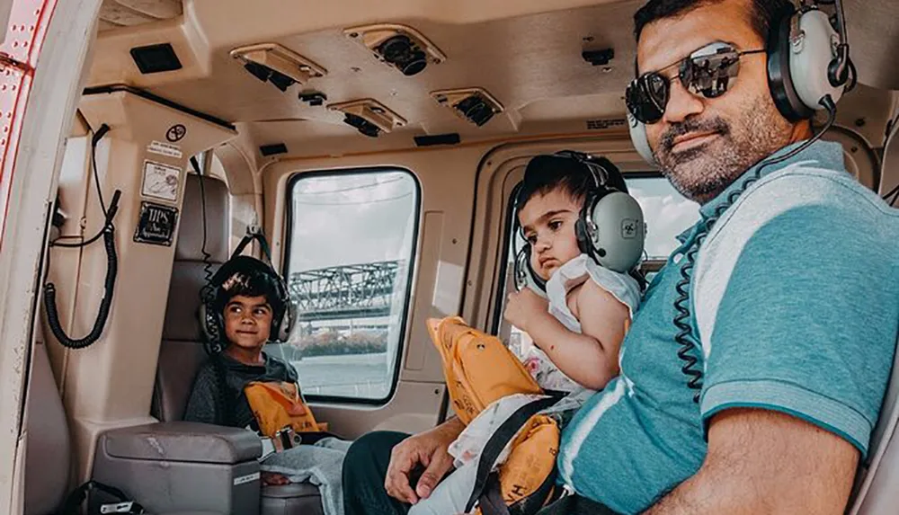A man and two children wearing headphones are seated inside a helicopter appearing ready for a flight