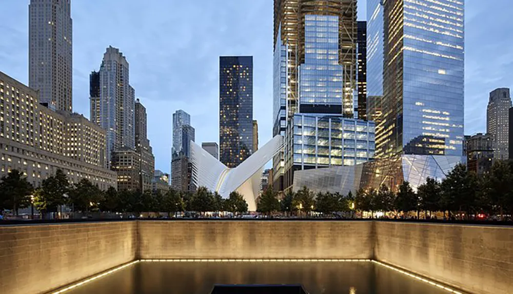 The image captures a serene twilight scene at a modern urban plaza with illuminated skyscrapers and a distinctive white building positioned adjacent to a reflective water feature