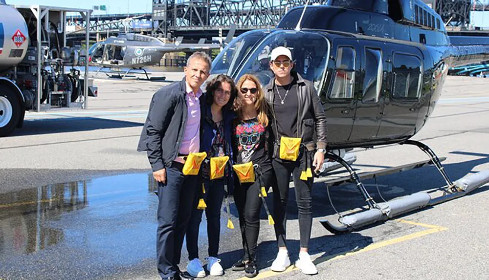 Four individuals are standing in front of a helicopter on a sunny day all wearing life vests and ready for a flight