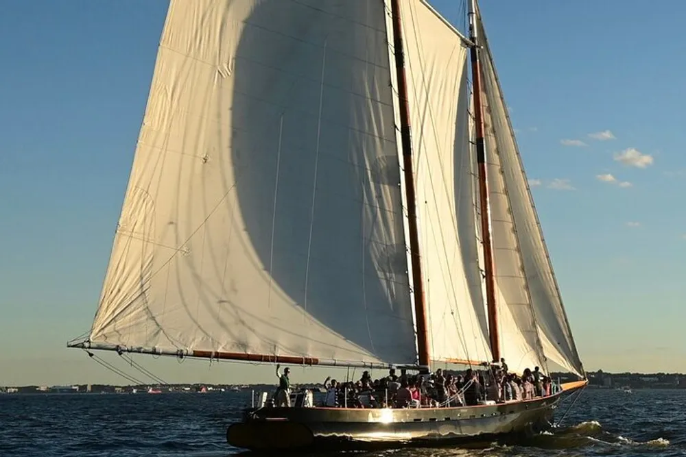 A group of people are enjoying a sail on a large traditional sailing yacht with its sails fully billowed in the late afternoon sun