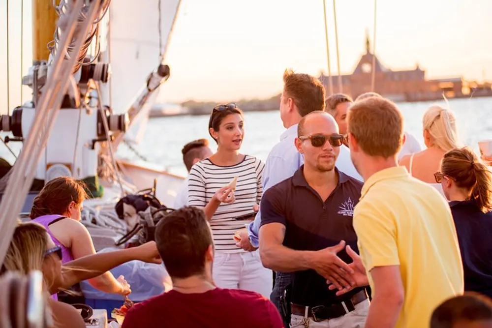 A group of people are socializing and enjoying themselves on a sailboat during a vibrant sunset