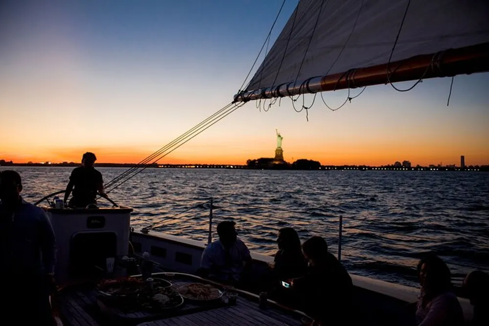 A group of people is enjoying an evening sail with a view of the Statue of Liberty at sunset