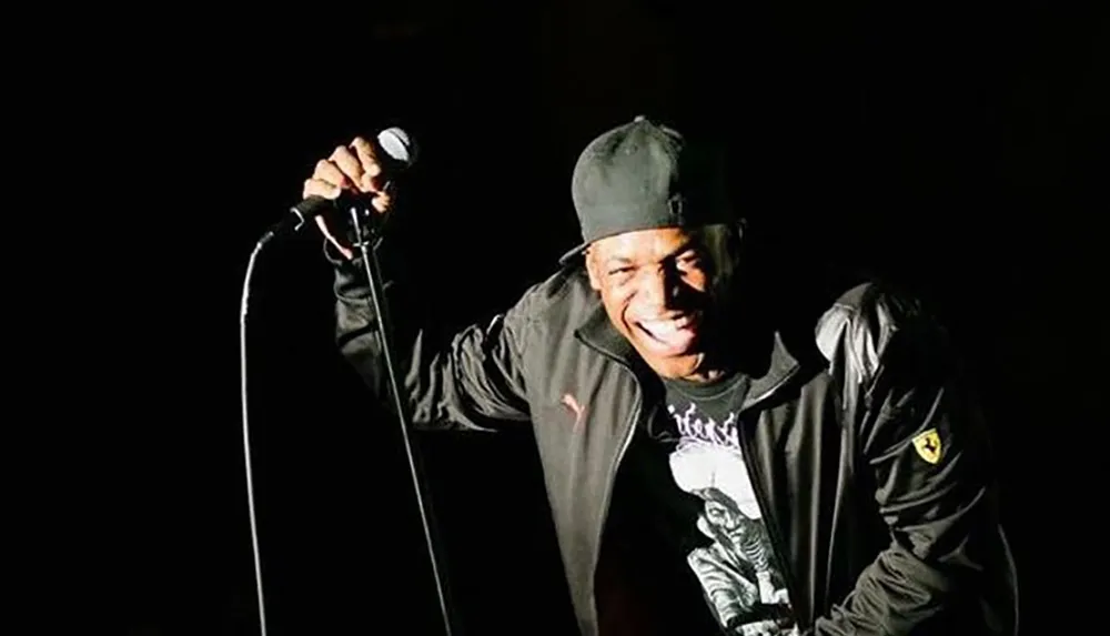 A person is joyfully performing on stage holding a microphone with a spotlight shining on them set against a dark background
