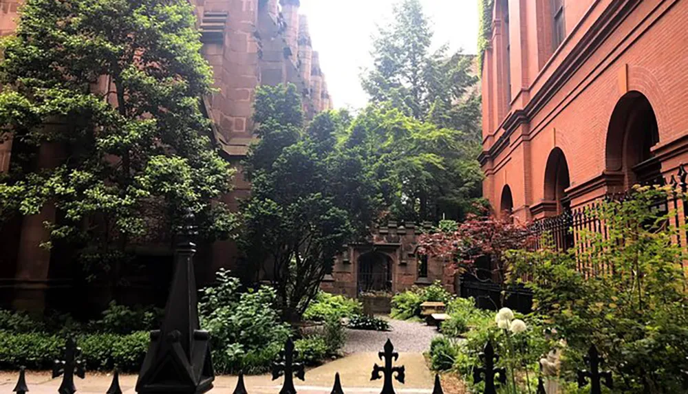 This image shows a tranquil courtyard garden with lush greenery ornate Gothic revival architectural details and a wrought iron fence providing a serene oasis amidst urban surroundings