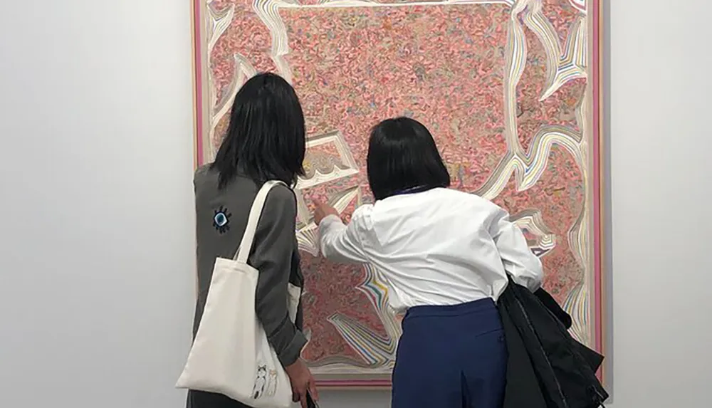 Two individuals are closely examining an intricately patterned artwork at a gallery