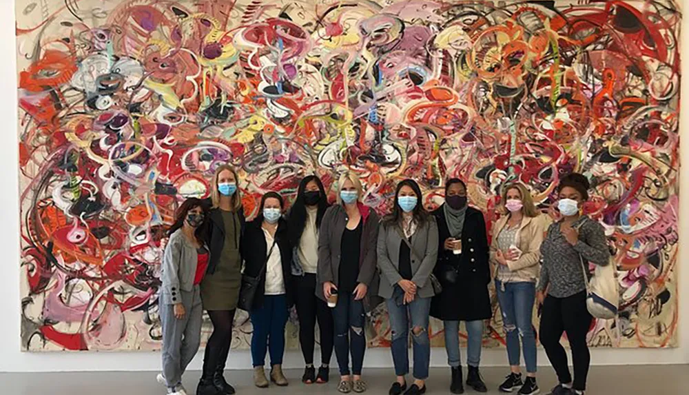 A group of people wearing face masks are posing for a photo in front of a large abstract painting