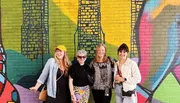 Four people are smiling in front of a colorful graffiti wall.