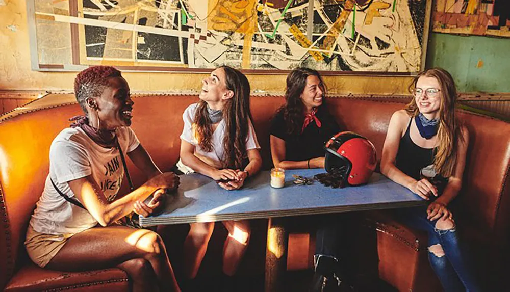 Four women appear to be enjoying a lively conversation in a cozy booth at a casual artsy cafe