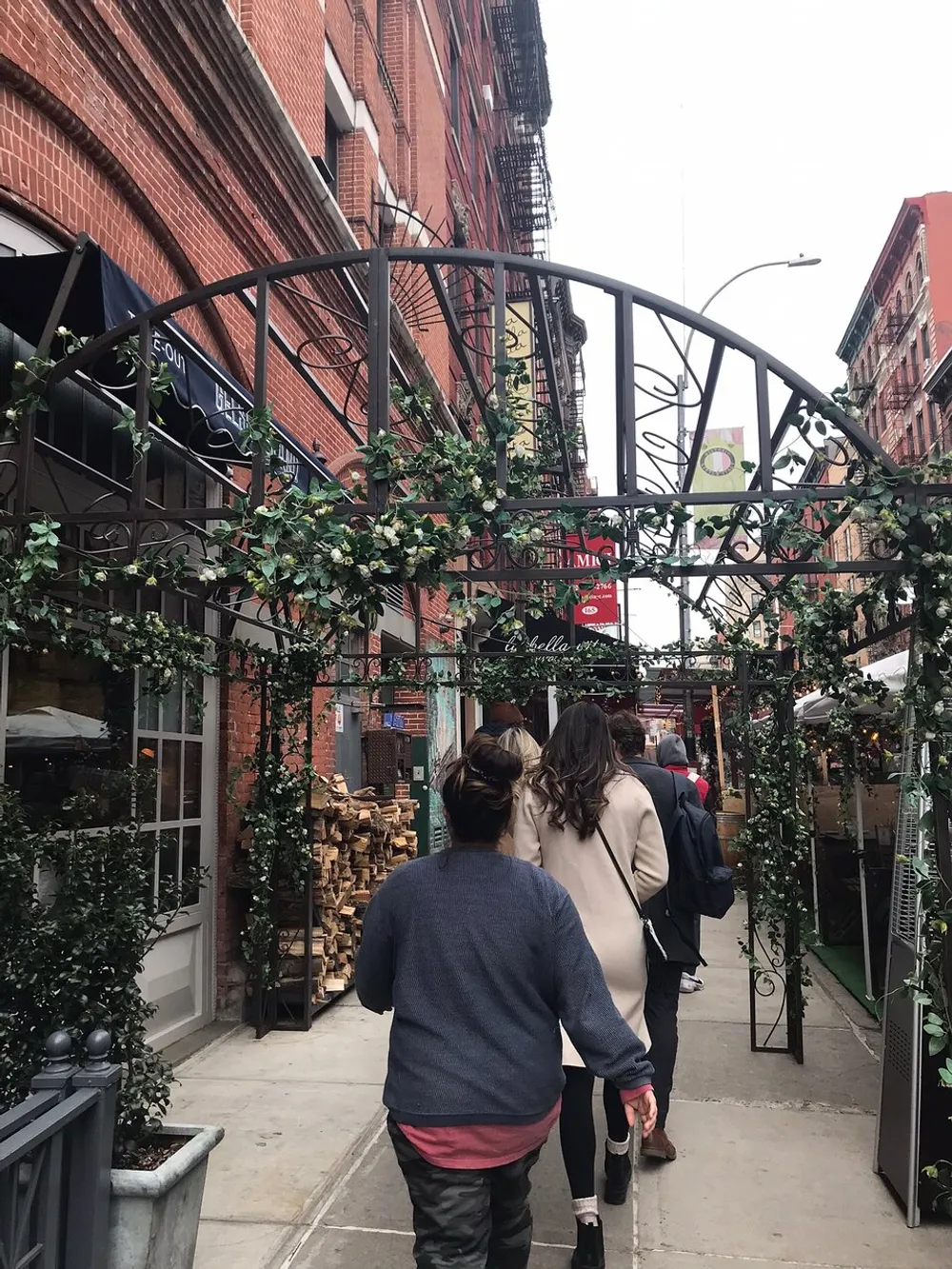 People walk down a charming city street adorned with a decorative vine-covered archway giving a cozy ambiance