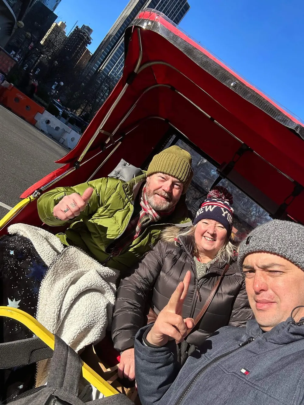 Three individuals are smiling and posing for a selfie while seated in a red horse-drawn carriage with one person making a peace sign