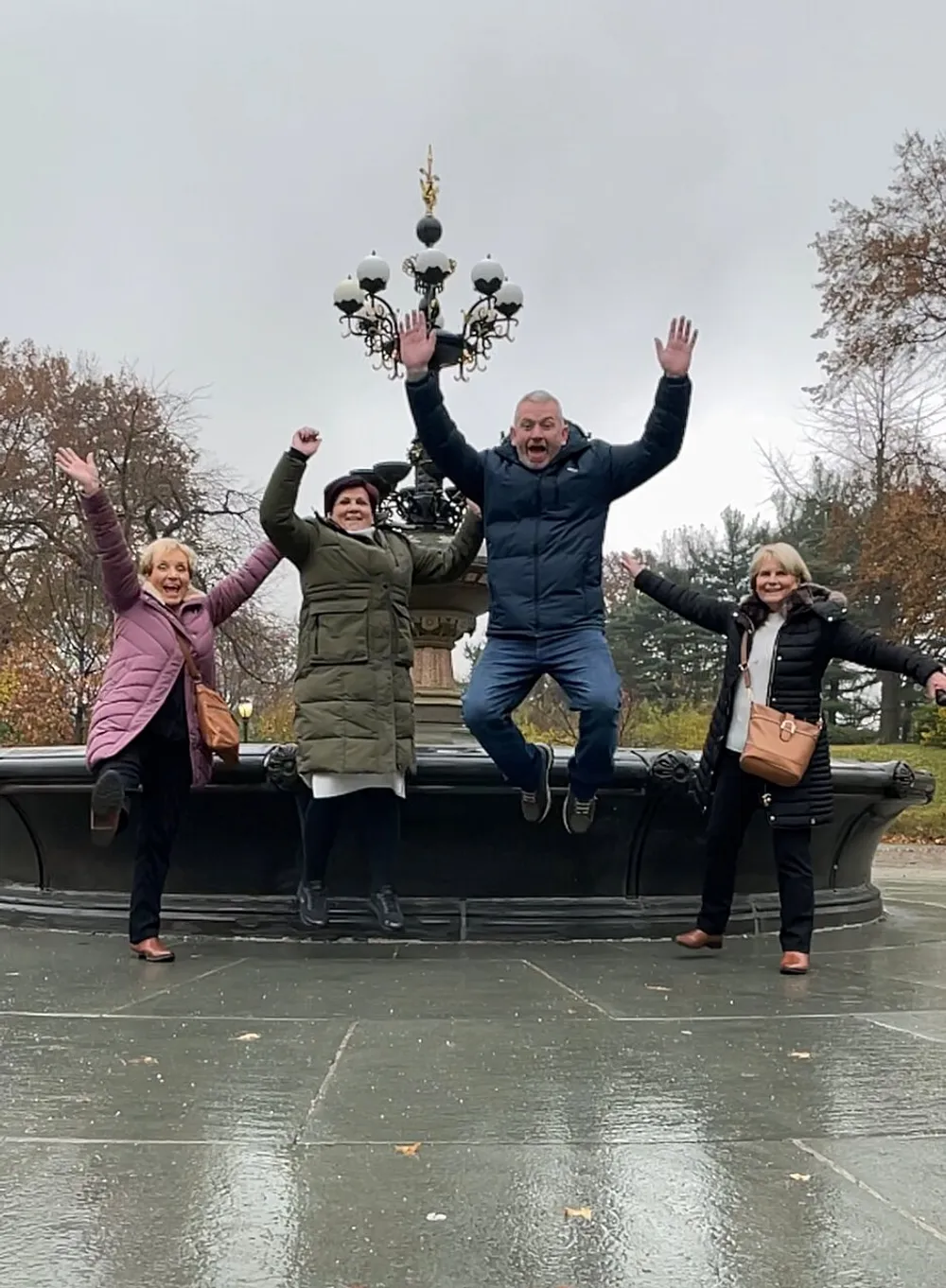 Four people are cheerfully posing with raised arms and jumping in front of an ornate lamp post capturing a moment of joy