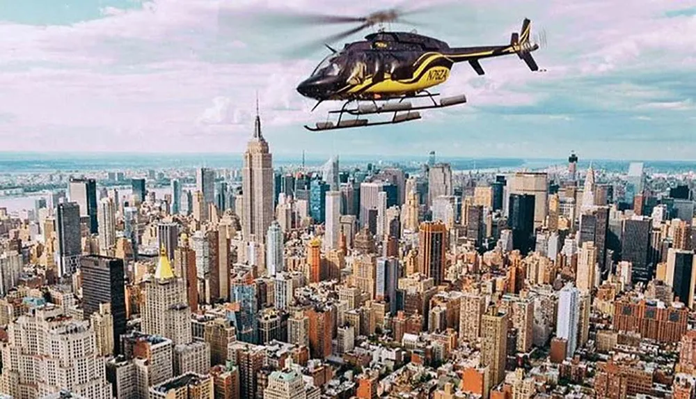 A yellow and black helicopter is flying over the New York City skyline featuring the Empire State Building