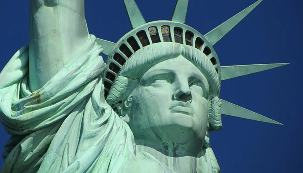 The image shows a close-up view of the face of the Statue of Liberty against a clear blue sky