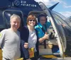 Two people are posing for a photo beside a smiling helicopter pilot who is giving a thumbs up from the helicopters cockpit