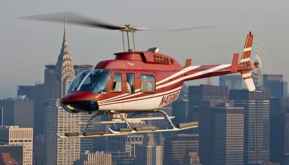 A red and white helicopter is flying in the foreground with a blurred city skyline in the background